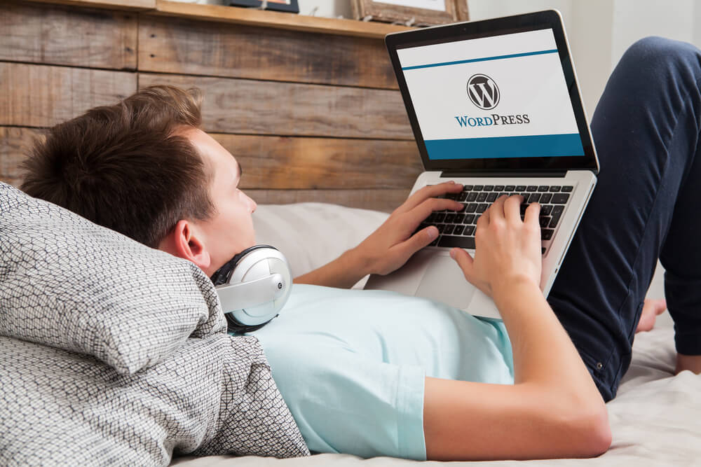 homem deitado em cama acessando no laptop site wordpress