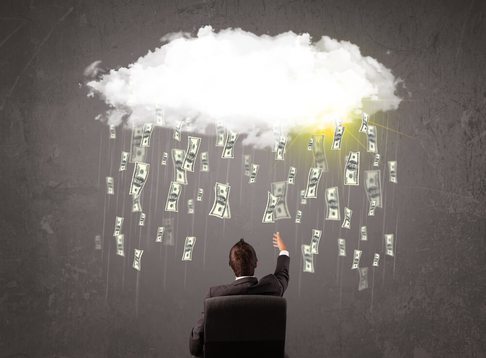 homem executivo sentado em cadeira apontando para representação de nuvem chovendo cédulas de dinheiro