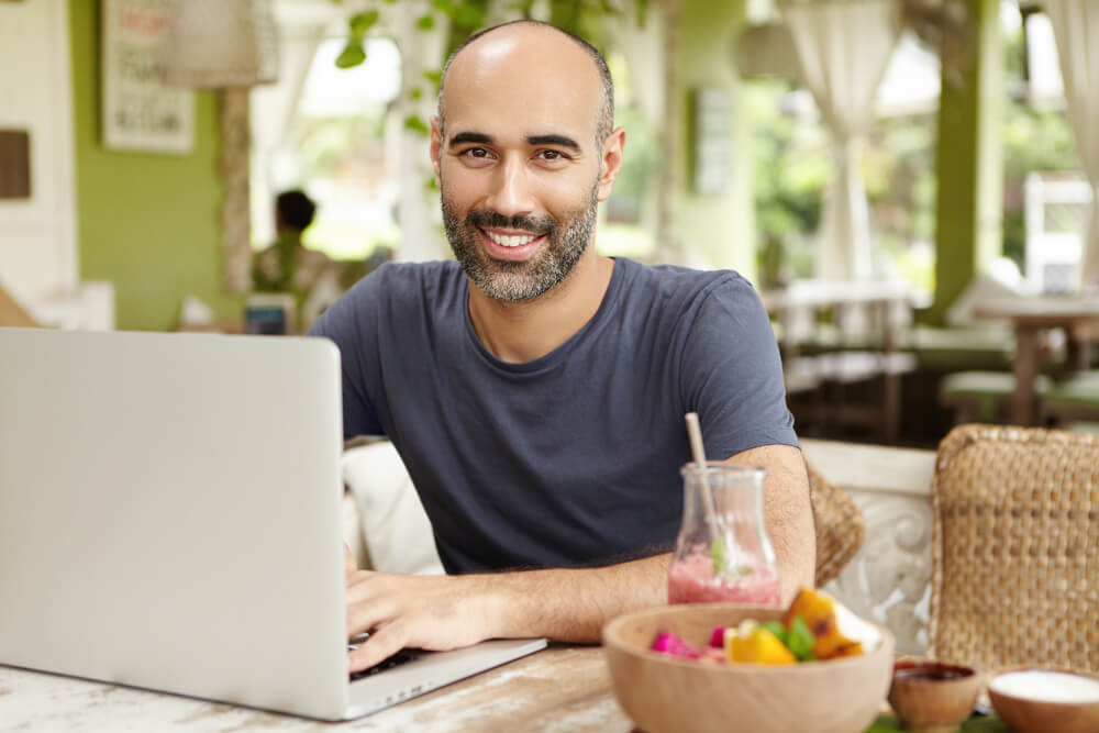 homem sorridente trabalhando em laptop em local informal