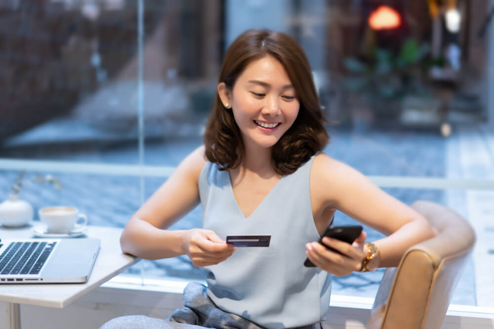 moça sorridente com smartphone e cartão de crédito