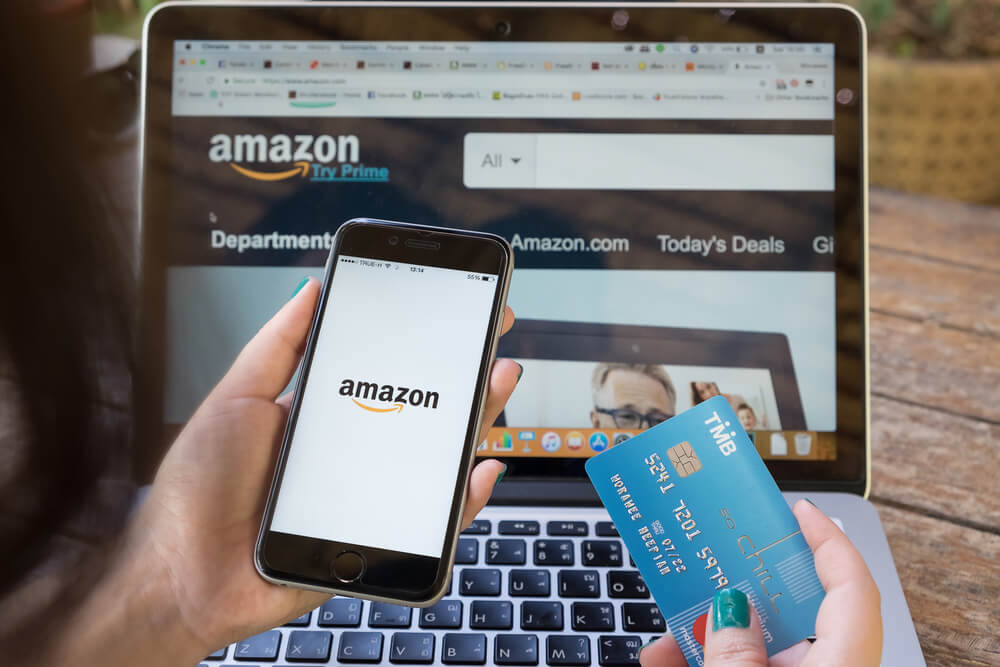 página da WEB e aplicativo mobile da Amazon em notebook, celular e um cartão de crédito