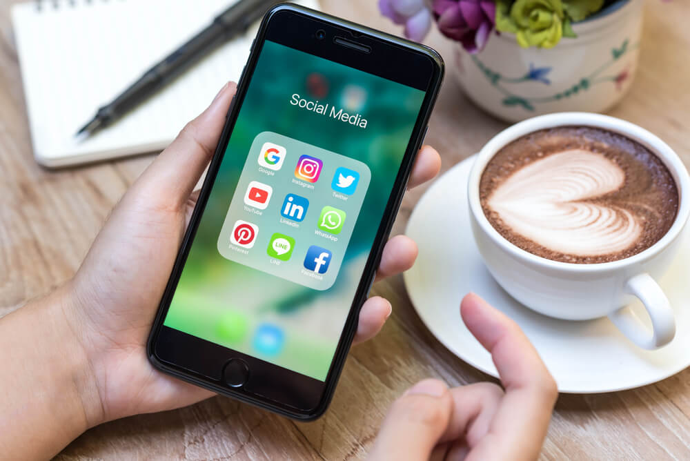smartphone na tela da pasta de midias sociais em mesa com xícara de café