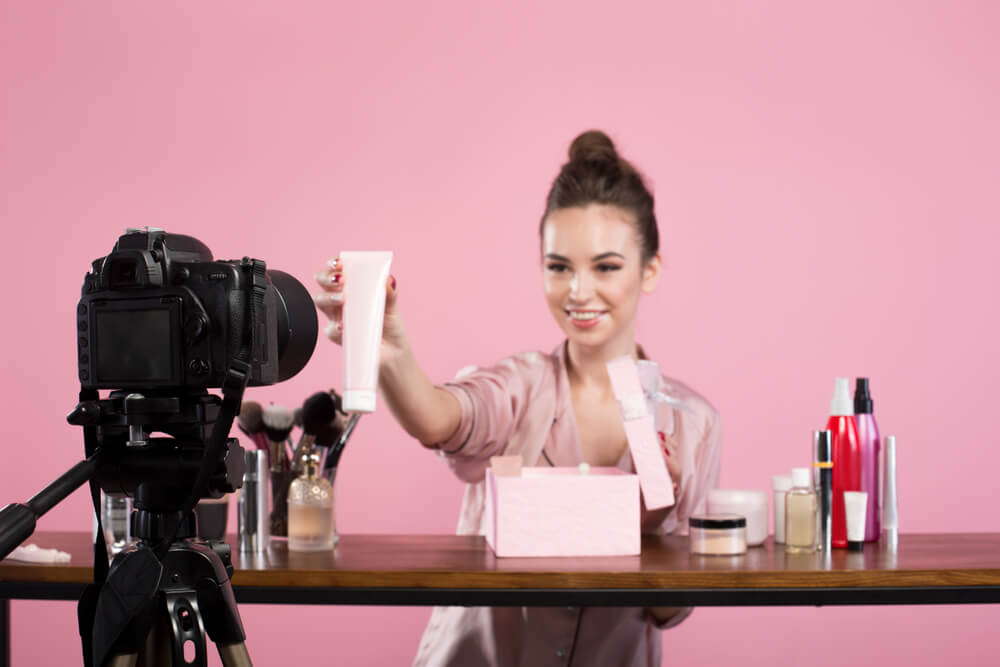 blogueira criando conteudo de video mostrando produtos de beleza em frente a camera profissional