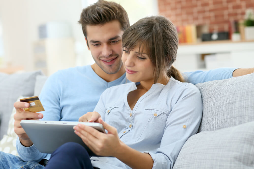 casal acessando laptop junto de cartão de crédito em mãos