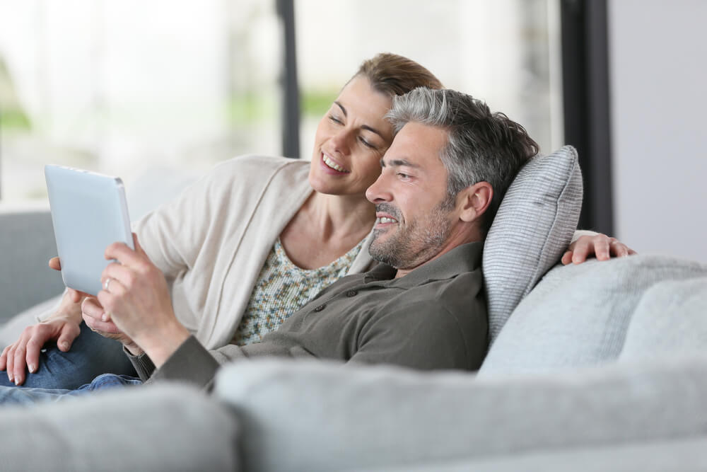 casal sentado em sofá em contato com a era digital por meio de uma tablet