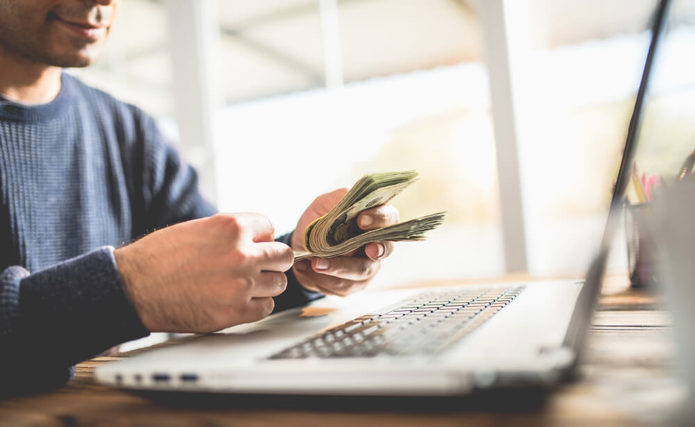 digital influencer segurando notas de dinheiro em frente a um laptop