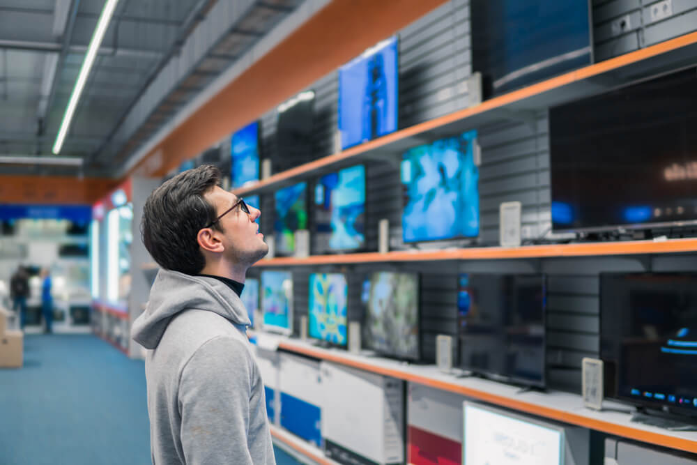 homem em loja física em processo de decisão de compra de uma TV
