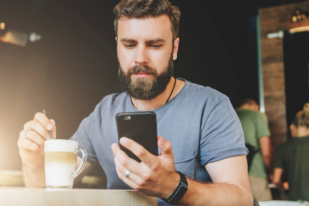 homem tomando café acessando smartphone