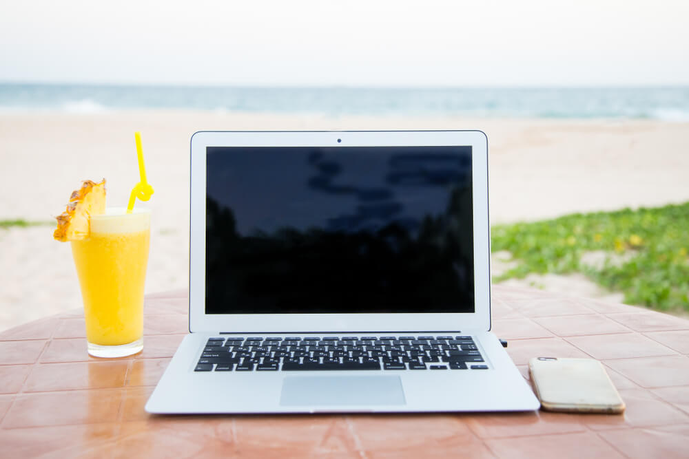 laptop com copo ao lado em cenario de praia