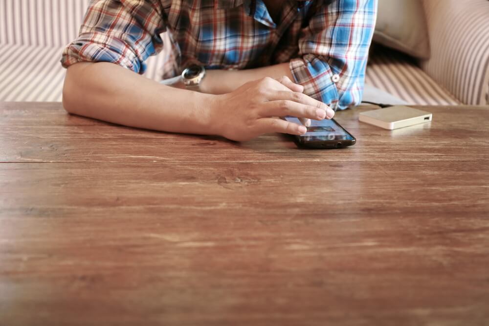mão masculina acessando smartphone em mesa de madeira