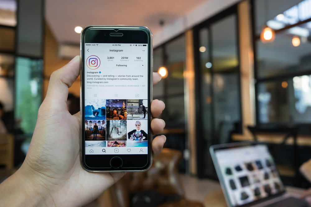 mao masculina segurando smartphone em perfil do aplicativo instagram em meio a local publico