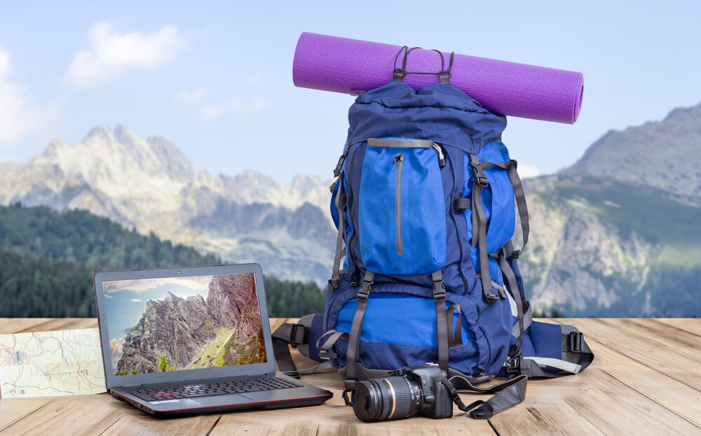 mochila de viajante, camera e laptop em cenario de montanhas