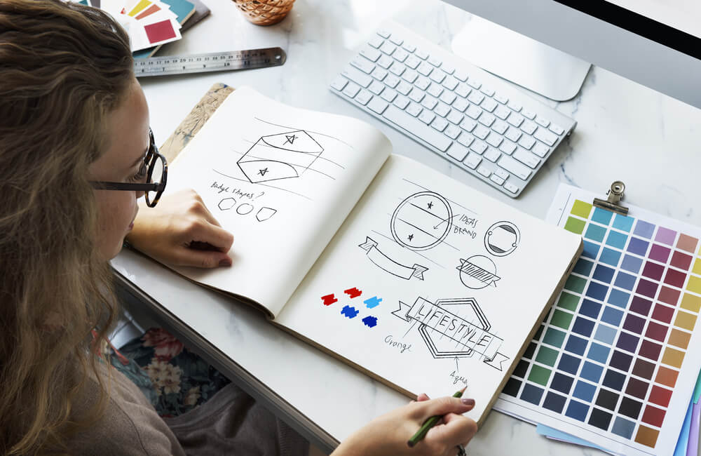 mulher em mesa de trabalho e rascunhos de logotipos criativos e manual de cores