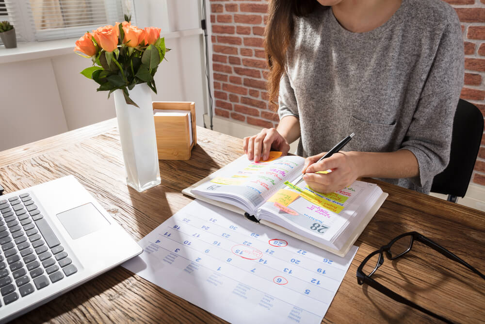 mulher fazendo anotações em agenda junto de calendario der planejamento