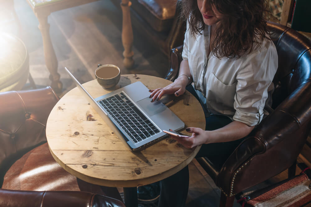 mulher trabalahndo em laptop junto de caneca de café em mesa informal