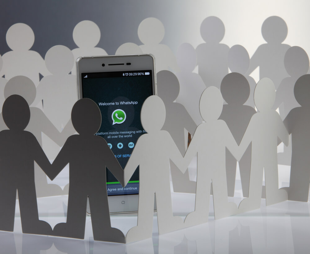smartphone com icone do aplicativo whatsapp e ilustraçao de bonecos de papel ao redor simbolizando grupos de whatsapp