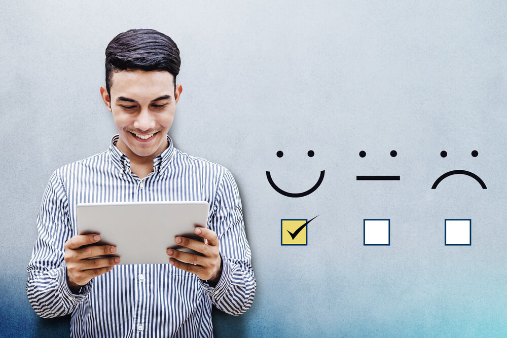 homem sorrindo ao olhar para tablet em suas maos e feedback positivo ao lado