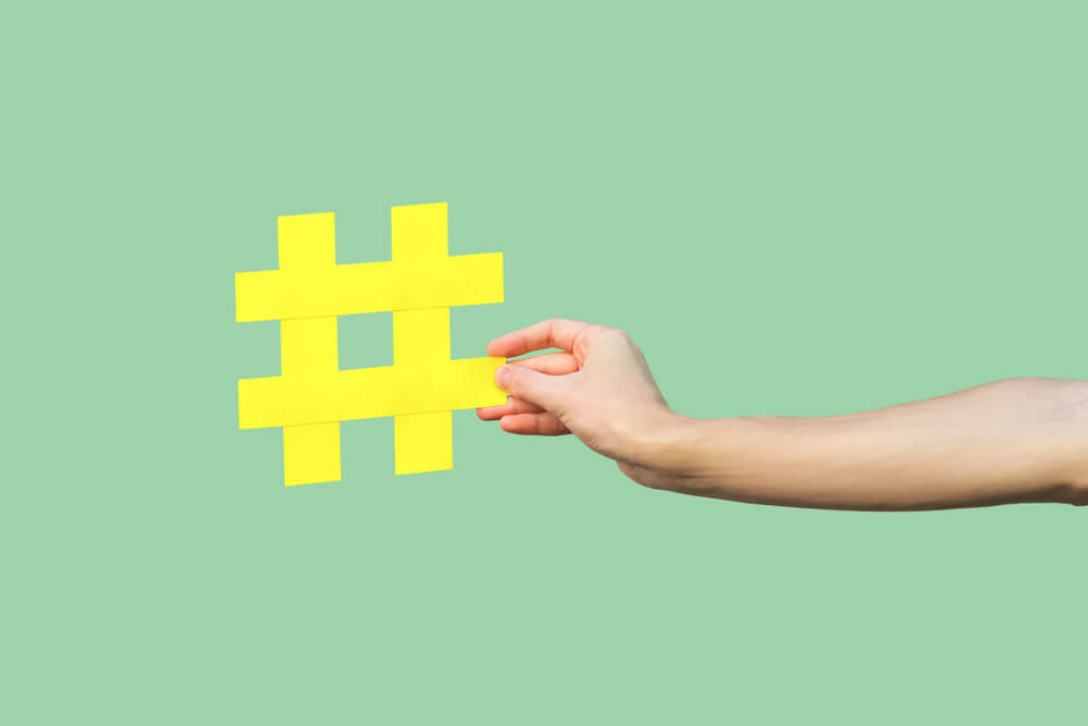 mão feminina segurando hashtag amarela em fundo verde