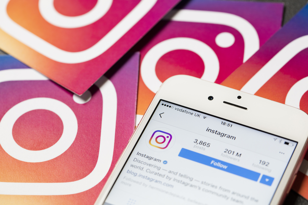 smartphone com perfil do aplicativo instagram em tela e icones de instagram ao fundo