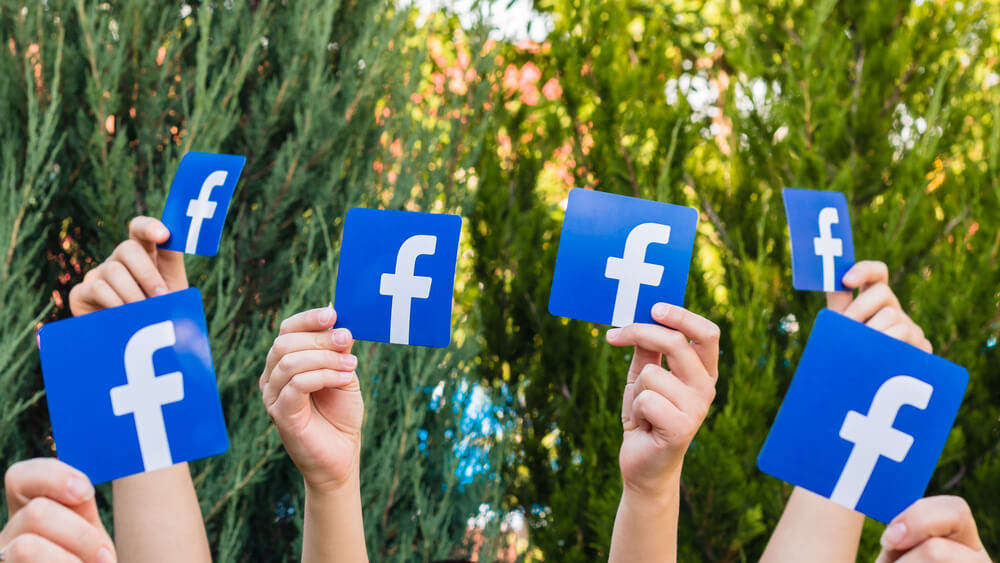 logos da rede social facebook sendo levantadas por mãos