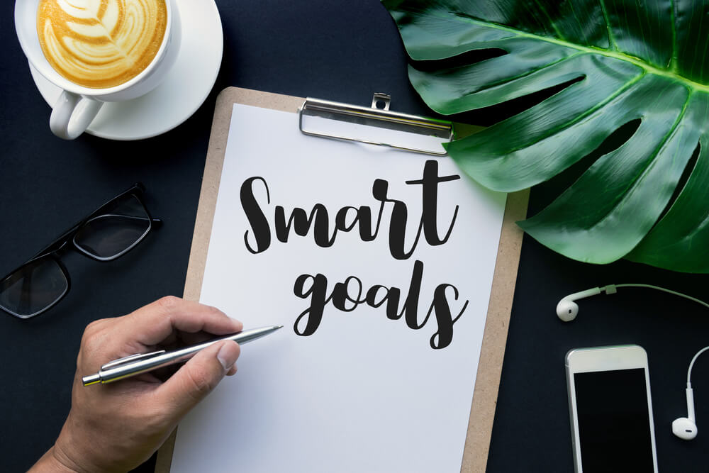 mão feminina escrevendo smart goals em prancheta