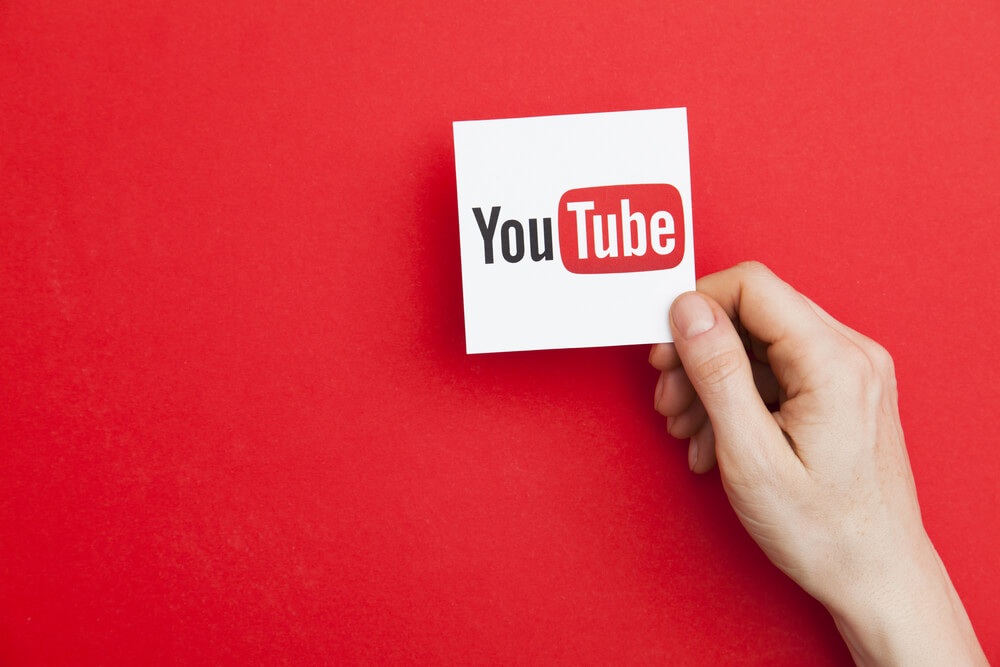 mao masculina segurando papel com icone do aplicativo youtube em fundo vermelho