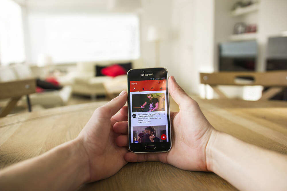 mao masculina segurando smartphone  em pagina inicial do aplicativo youtube e thumbnails de videos em tela