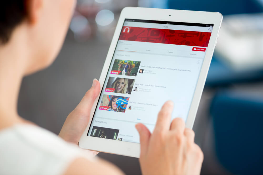 mulher segurando tablet em canal do aplicativo youtube com diversos videos e suas thumbnails em tela