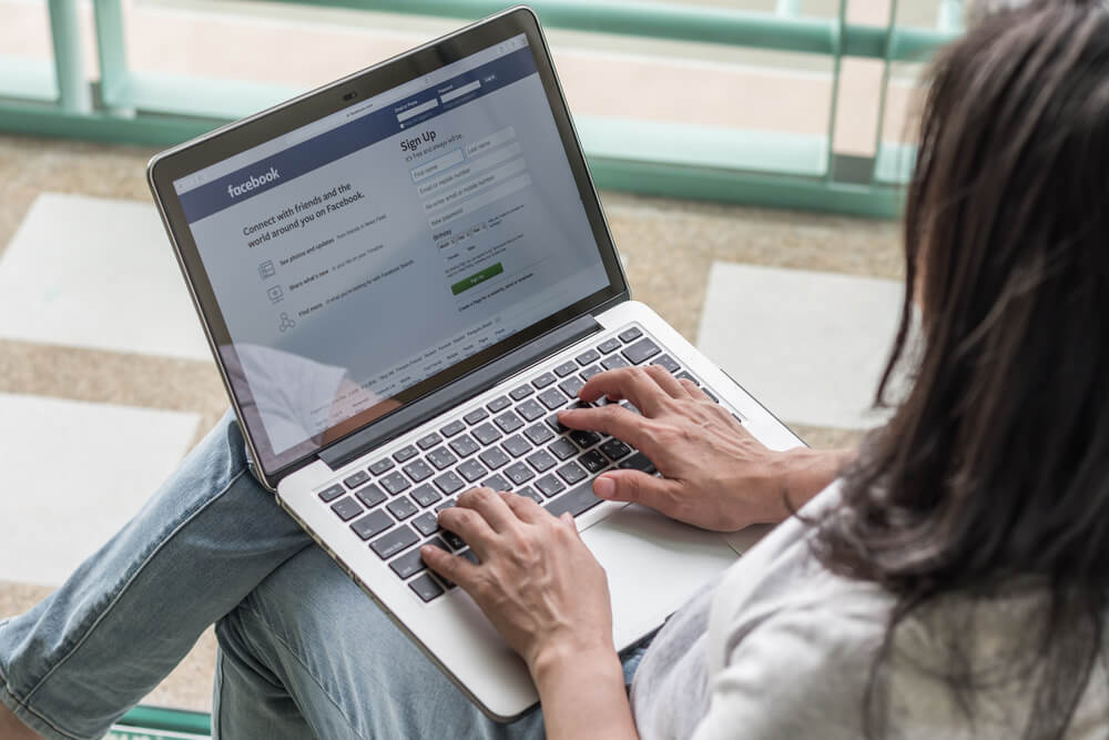 mulher sentada com laptop em colo em pagina de login do site facebook