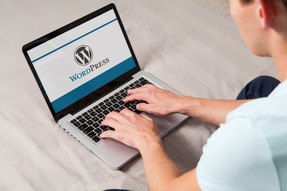homem teclando em laptop com logo da plataforma wordpress em tela