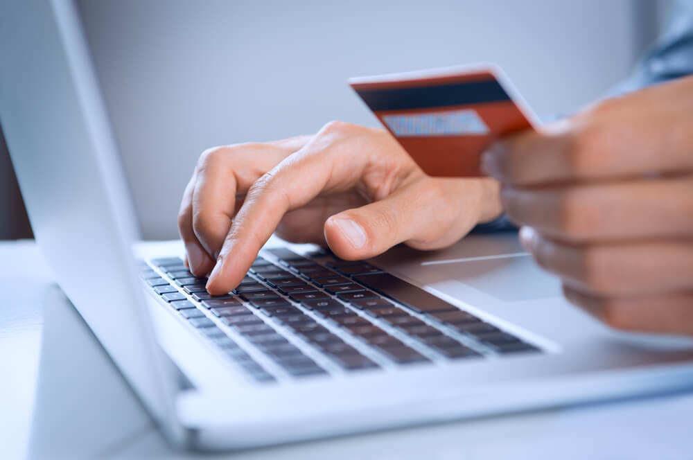 homem usando laptop e segurando cartao de credito simbolizando compras em e-commerce