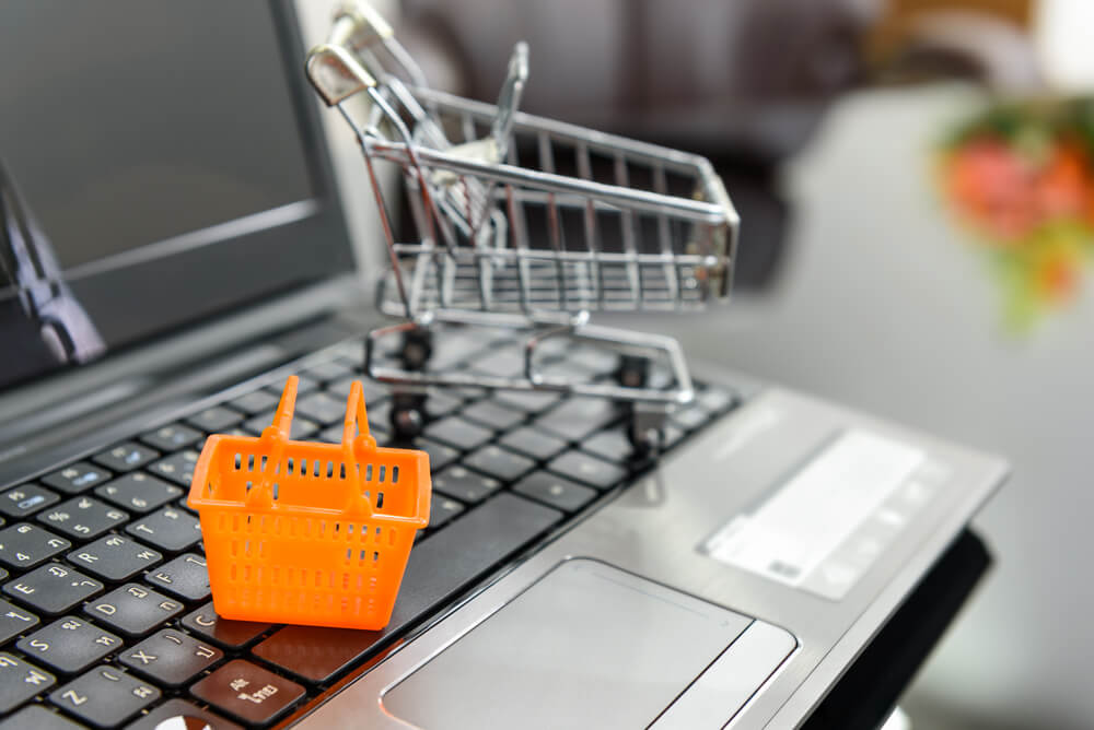 mini cesta de compras e mini carrinho de supermercado sob teclado de laptop simbolizando loja virtual