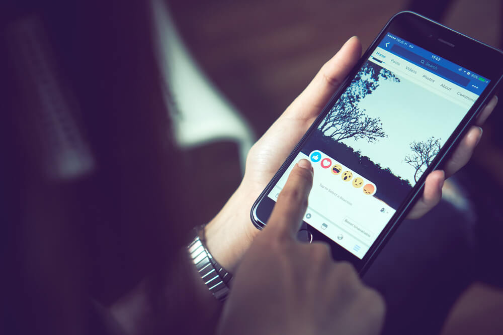 mulher com smartphone em maos com reaçoes de publicaçao do aplicativo facebook em tela
