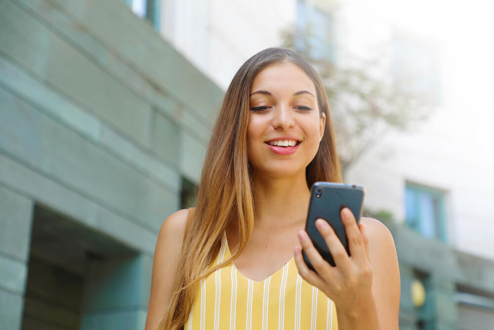 mulher sorrindo ao observar tela de smartphone