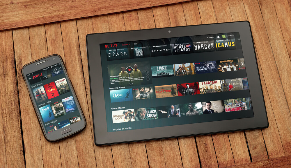 tablet e smartphone em mesa na plataforma netflix com diferentes thumbnails de filmes e series